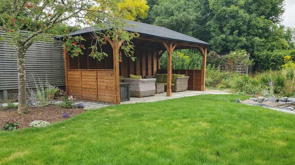 A beautiful wooden gazebo housing a seating area, behind a lush green lawn.
